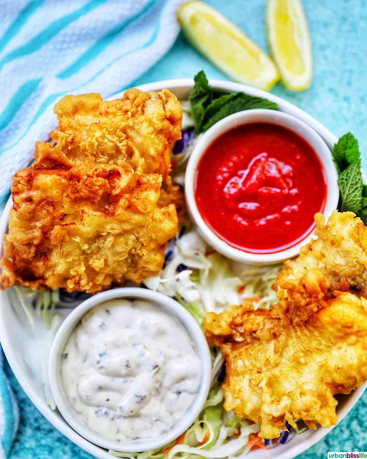 air fryer cod pieces on a plate with sides of tartar sauce, coleslaw, and cocktail sauce.