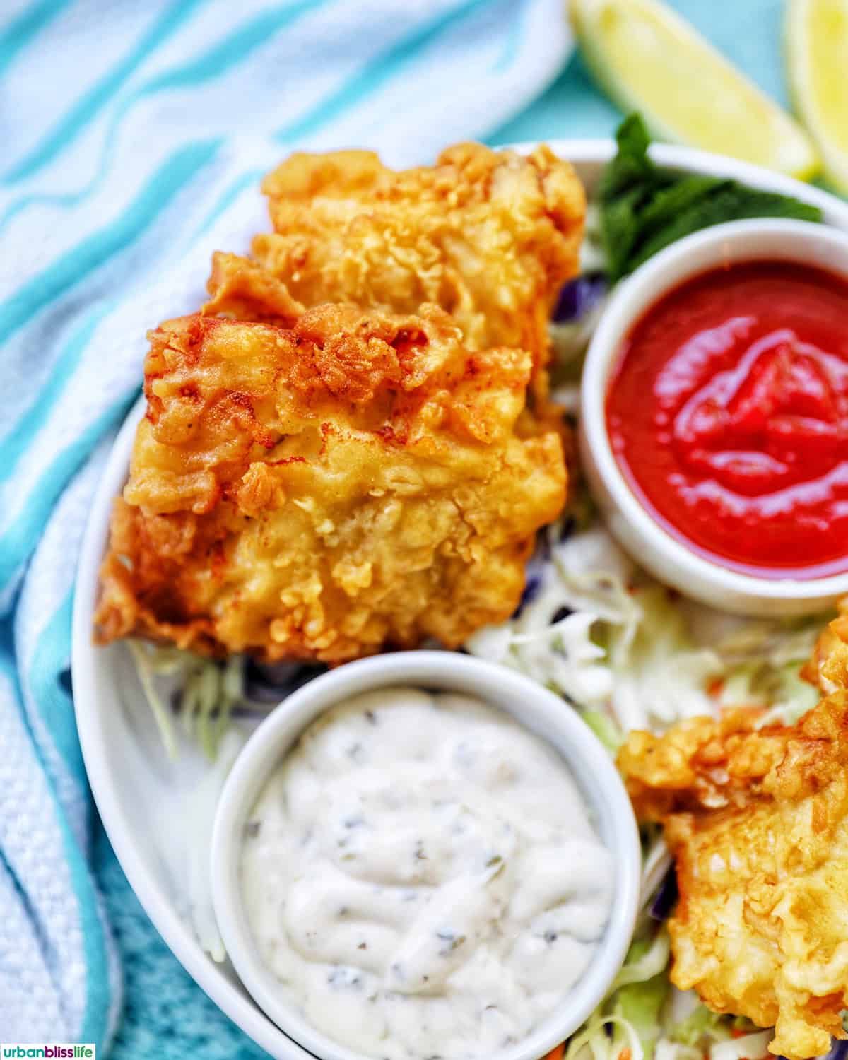air fryer cod pieces on a plate with sides of tartar sauce, coleslaw, and cocktail sauce.