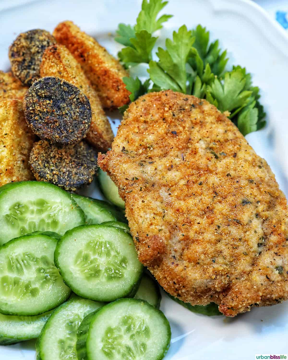 air fryer shake and bake pork chops on a white plate with cucumbers and potatoes.