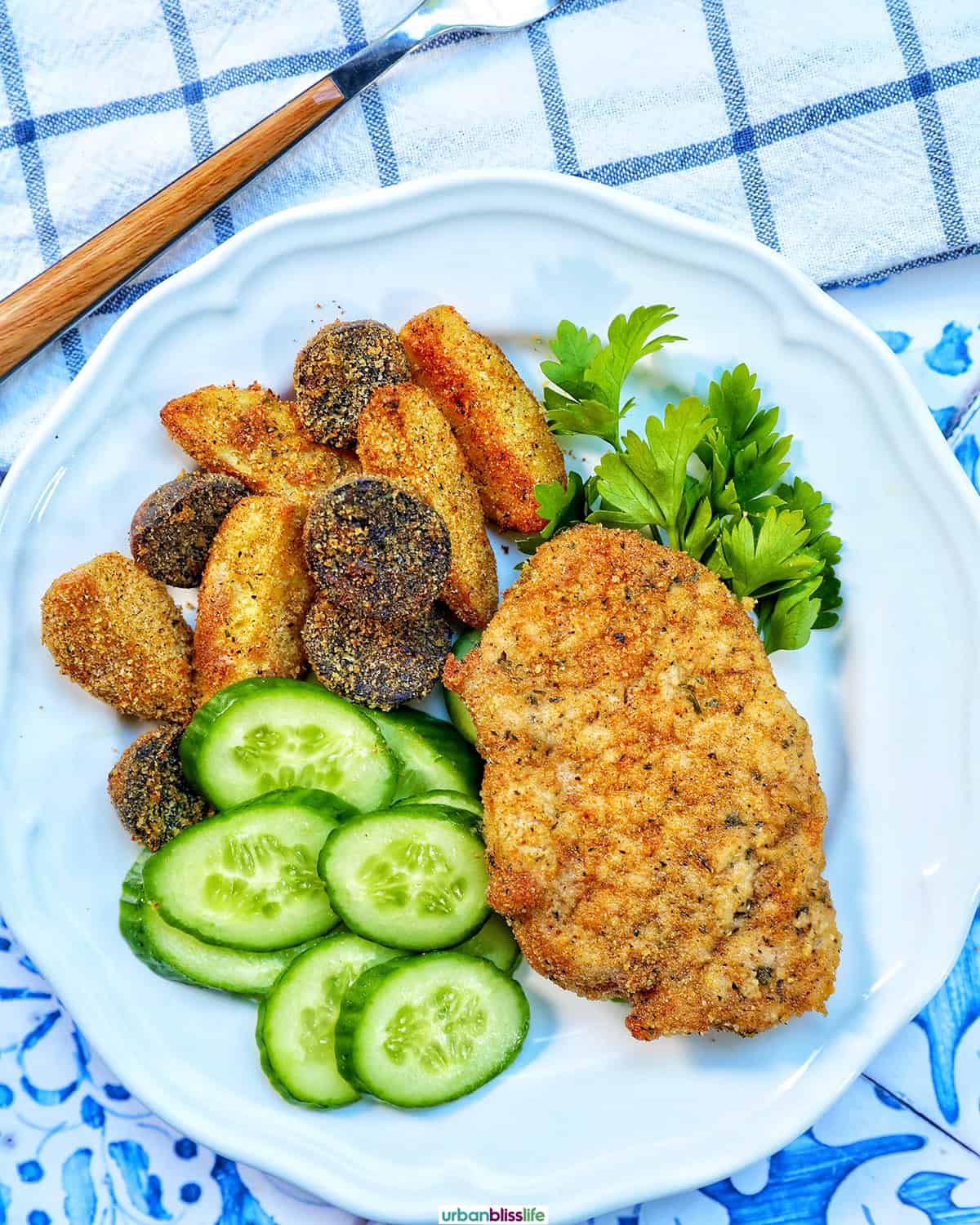 air fryer shake and bake pork chops on a white plate with cucumbers and potatoes.