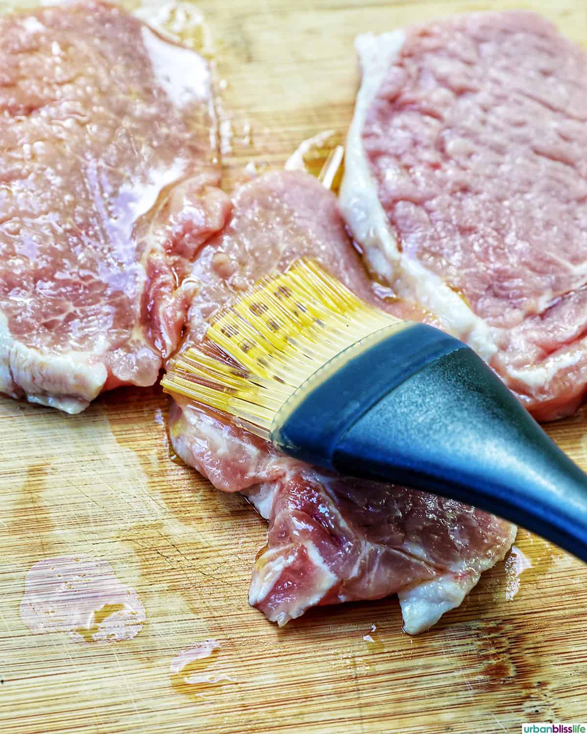 brushing olive oil on pork chops on a cutting board.