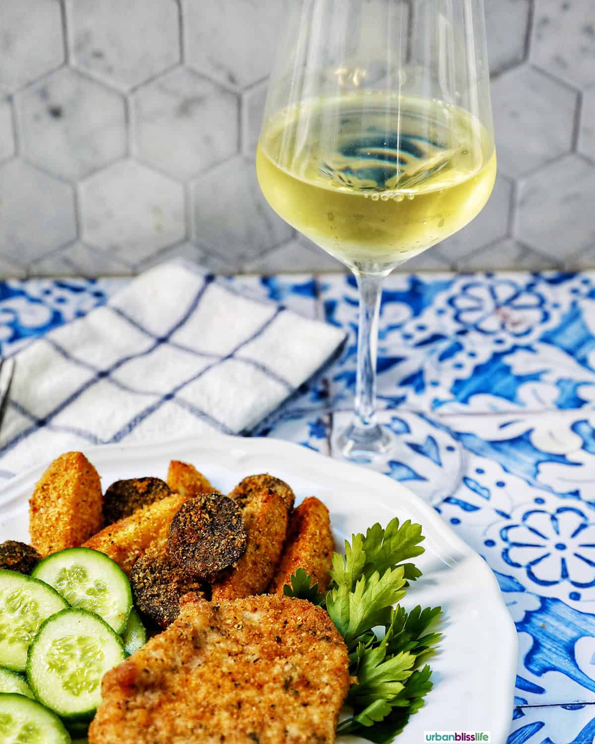 air fryer shake and bake pork chops on a white plate with cucumbers and potatoes and a glass of white wine.