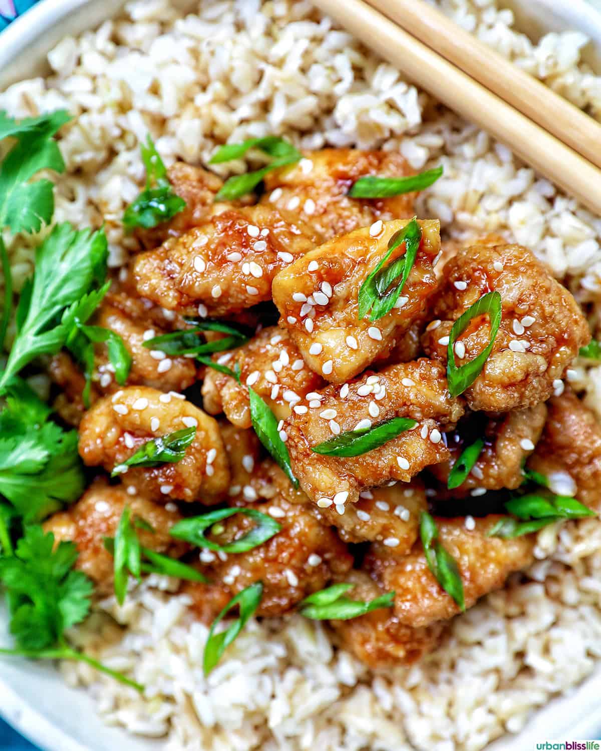 Air fryer teriyaki chicken over brown rice with herbs and chopsticks.