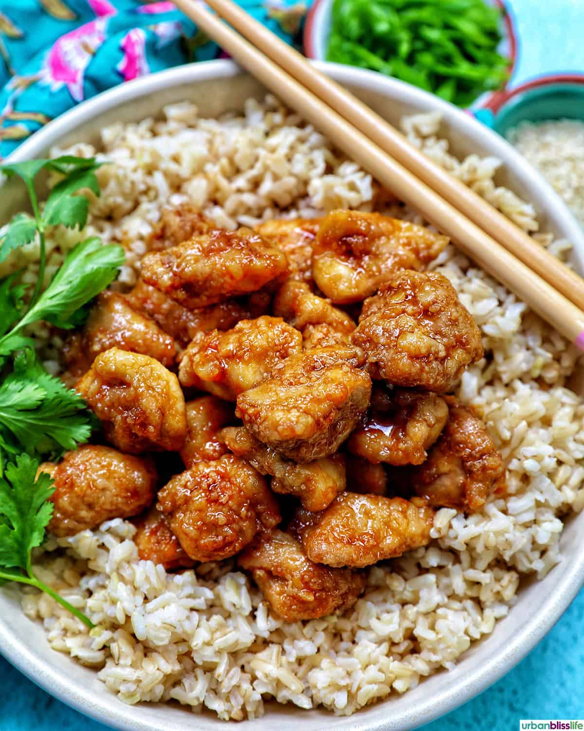 Air fryer teriyaki chicken over brown rice with herbs and chopsticks.