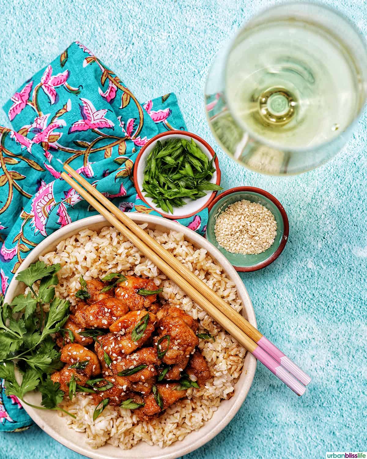 Air fryer teriyaki chicken over brown rice with herbs and chopsticks with a glass of white wine.