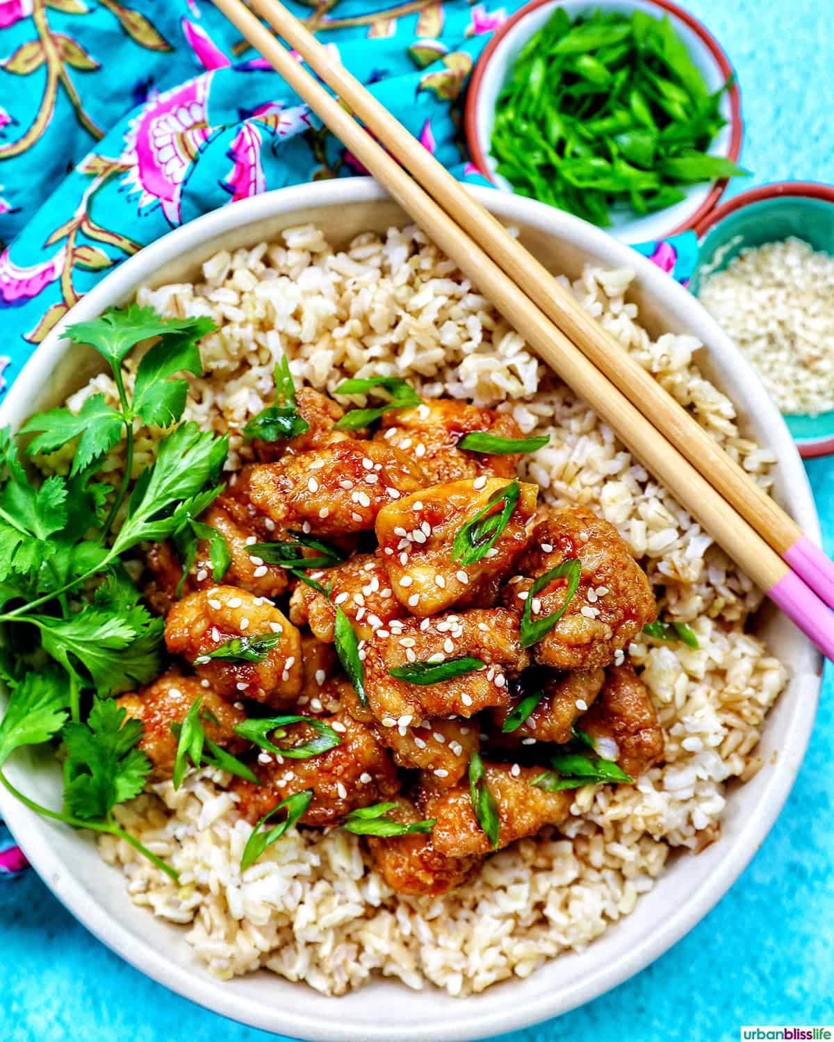 Air fryer teriyaki chicken over brown rice with herbs and chopsticks.