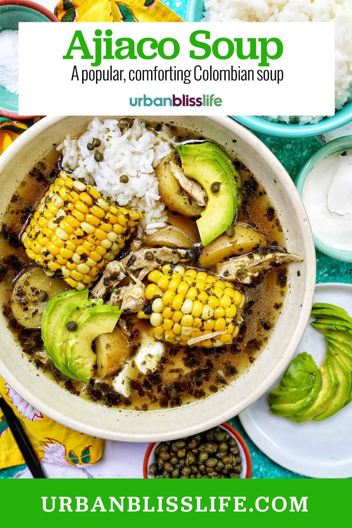 bowl of Colombian Ajiaco soup with corn on the cob and chicken, and sides of rice, avocado slices, capers, and sour cream with title text overlay.