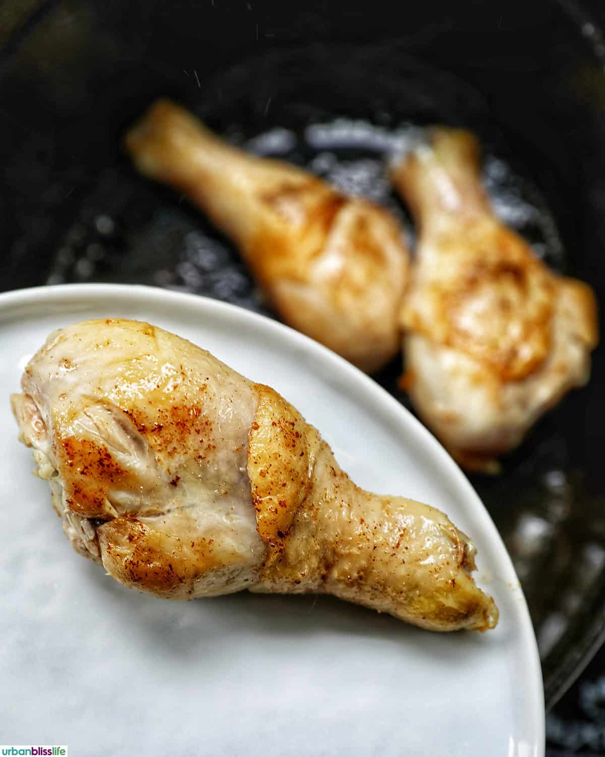 chicken pieces cooking in a dutch oven with one cooked piece on a plate.