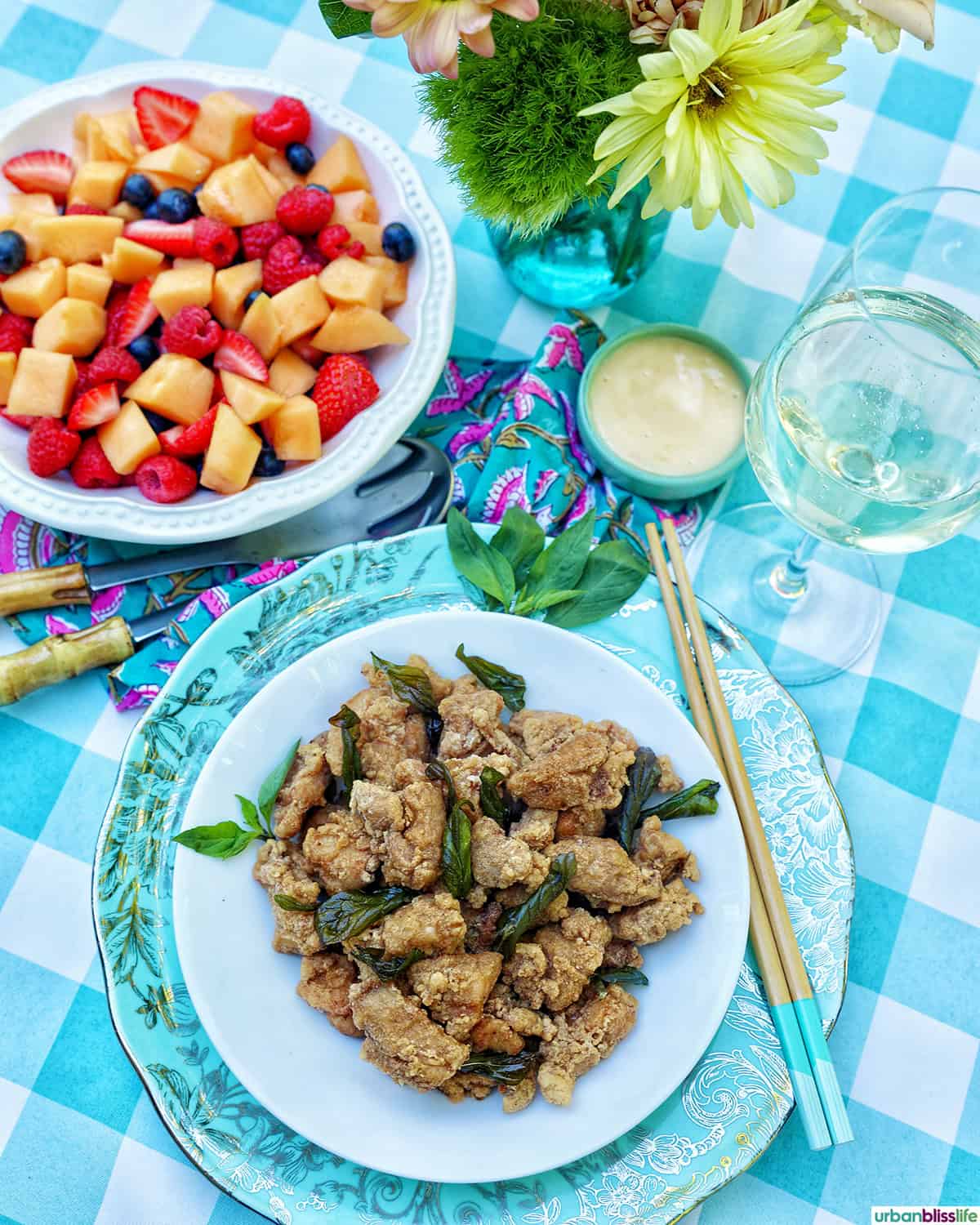 bowl of Taiwanese popcorn chicken and bowl of fruit salad and glass of white wine.
