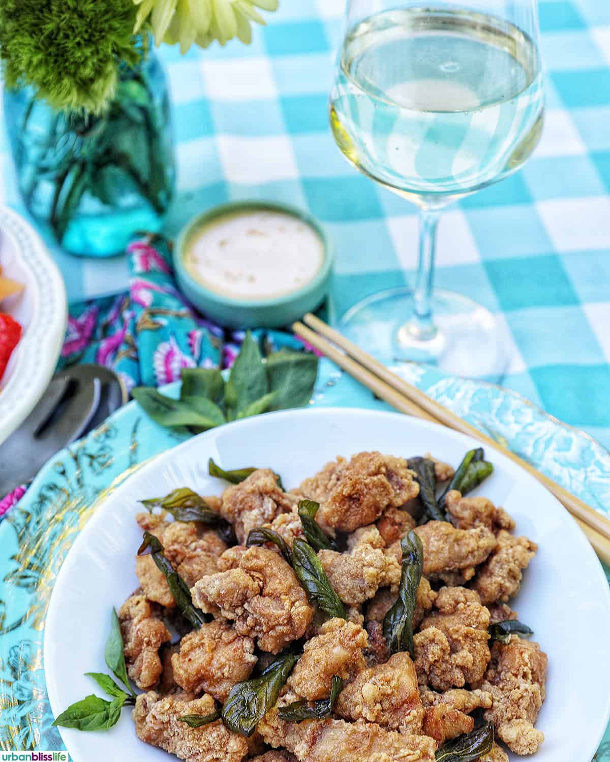 bowl of Taiwanese popcorn chicken with fried basil and glass of white wine.