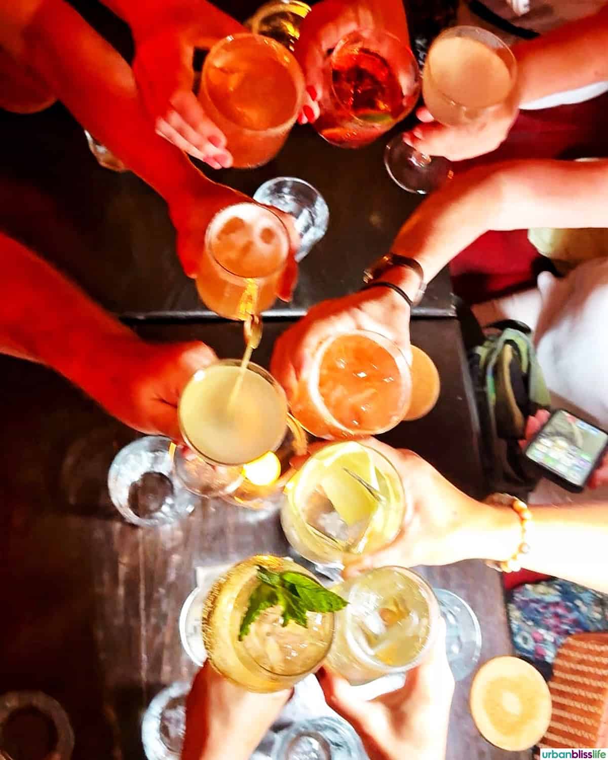 several hands holding cocktails at Alquimico bar in Cartagena, Colombia.