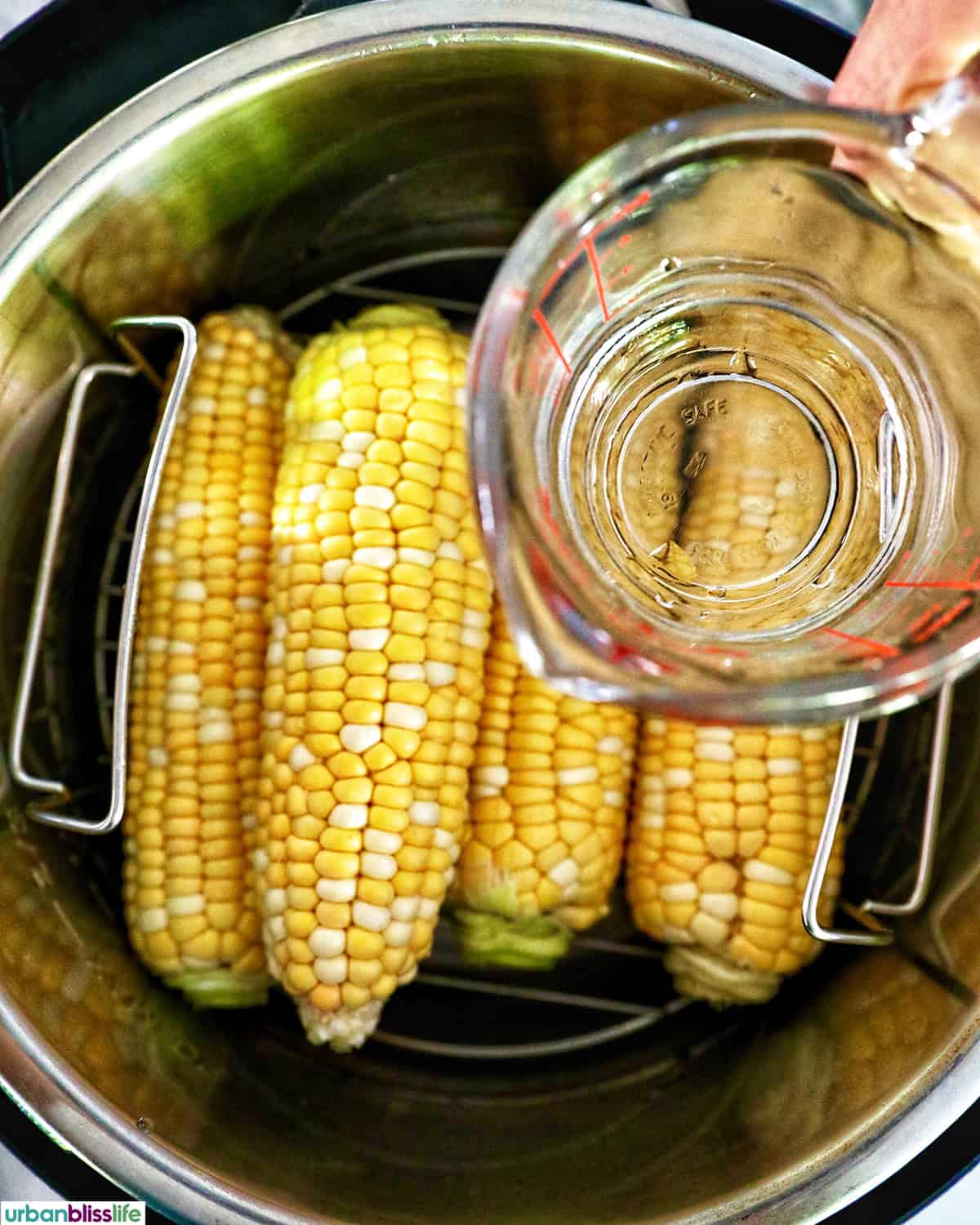 corn on the cob in an Instant Pot with a hand pouring water over it.