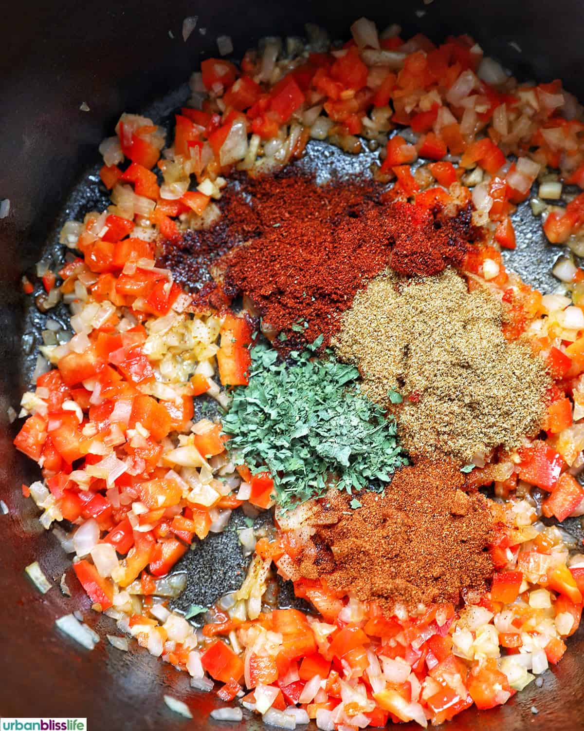 spices over vegetables in a pot to make vegan three bean chili.