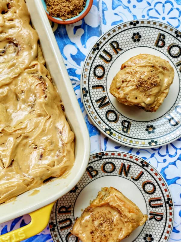 baking dish with coffee cinnamon rolls against a blue and white French backdrop and two plates with cinnamon rolls on them.