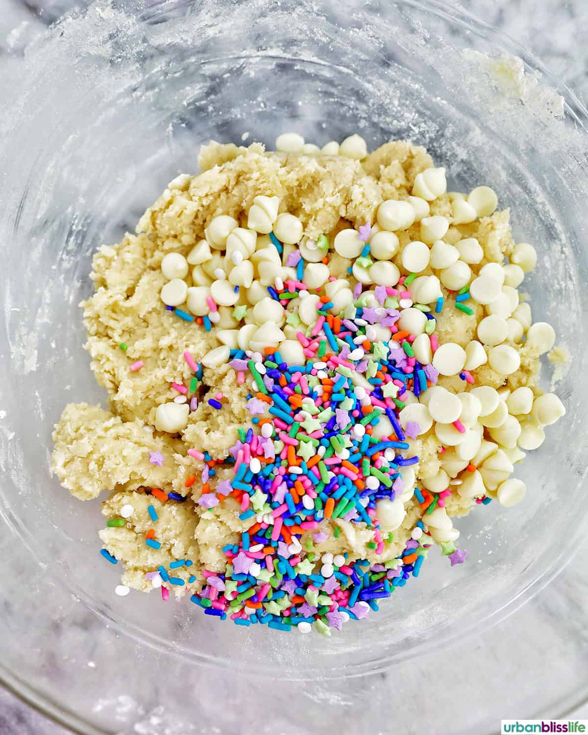 white chocolate chips and colorful sprinkles added to Sugar Cookie Confetti Cake in a bowl.
