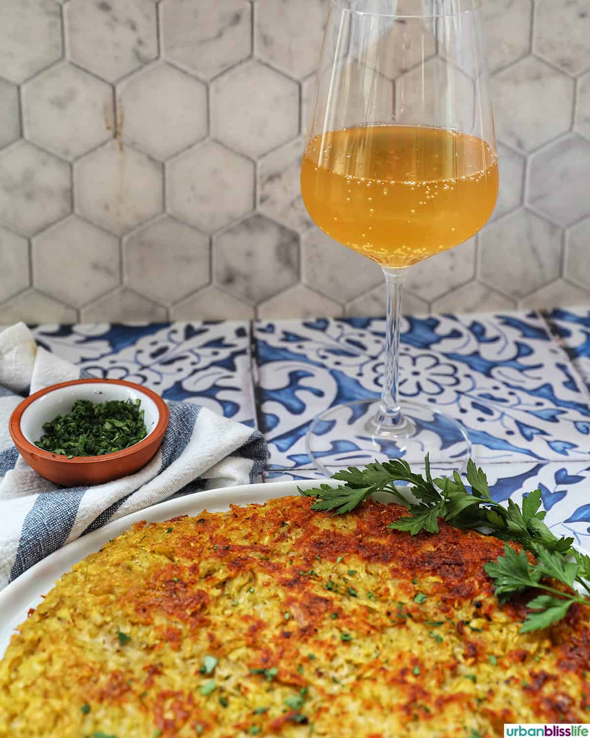 Swiss Rosti on a plate with glass of Pet Nat sparkling wine and parsley garnish.