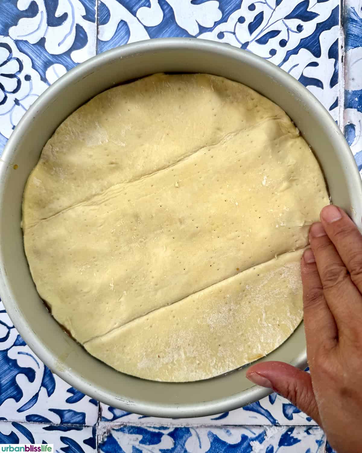 hand pressing a layer of puff pastry on top of a pomme tarte tatin.