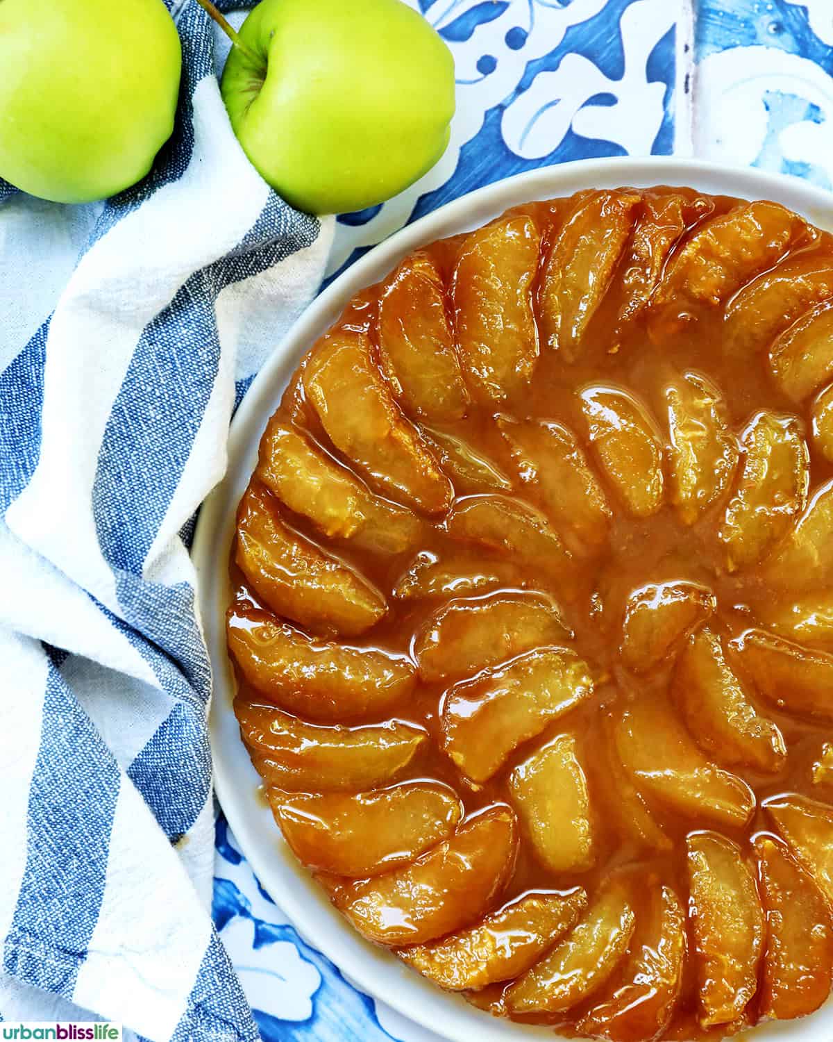 overhead photo of a closeup of a Pomme Tarte Tatin apple tart with two apples next to it.